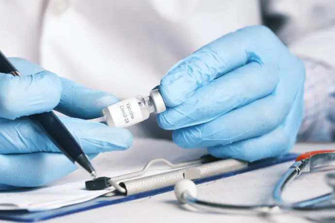 Hände in blauen Handschuhen die eine Impfdosis hält
