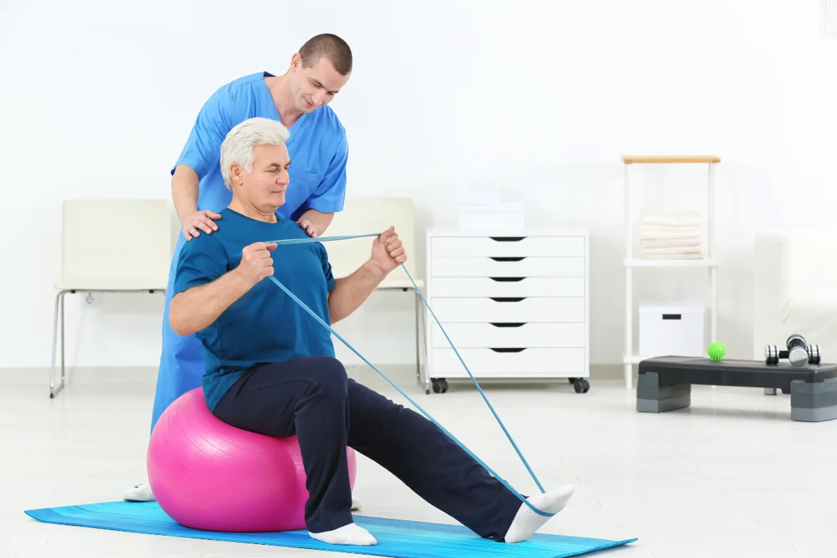 Therapeut mit Patient auf Gymnastikball, Theraband